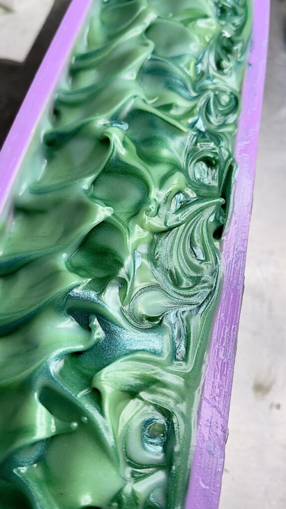 A close up of the green and purple paint on a piece of wood.